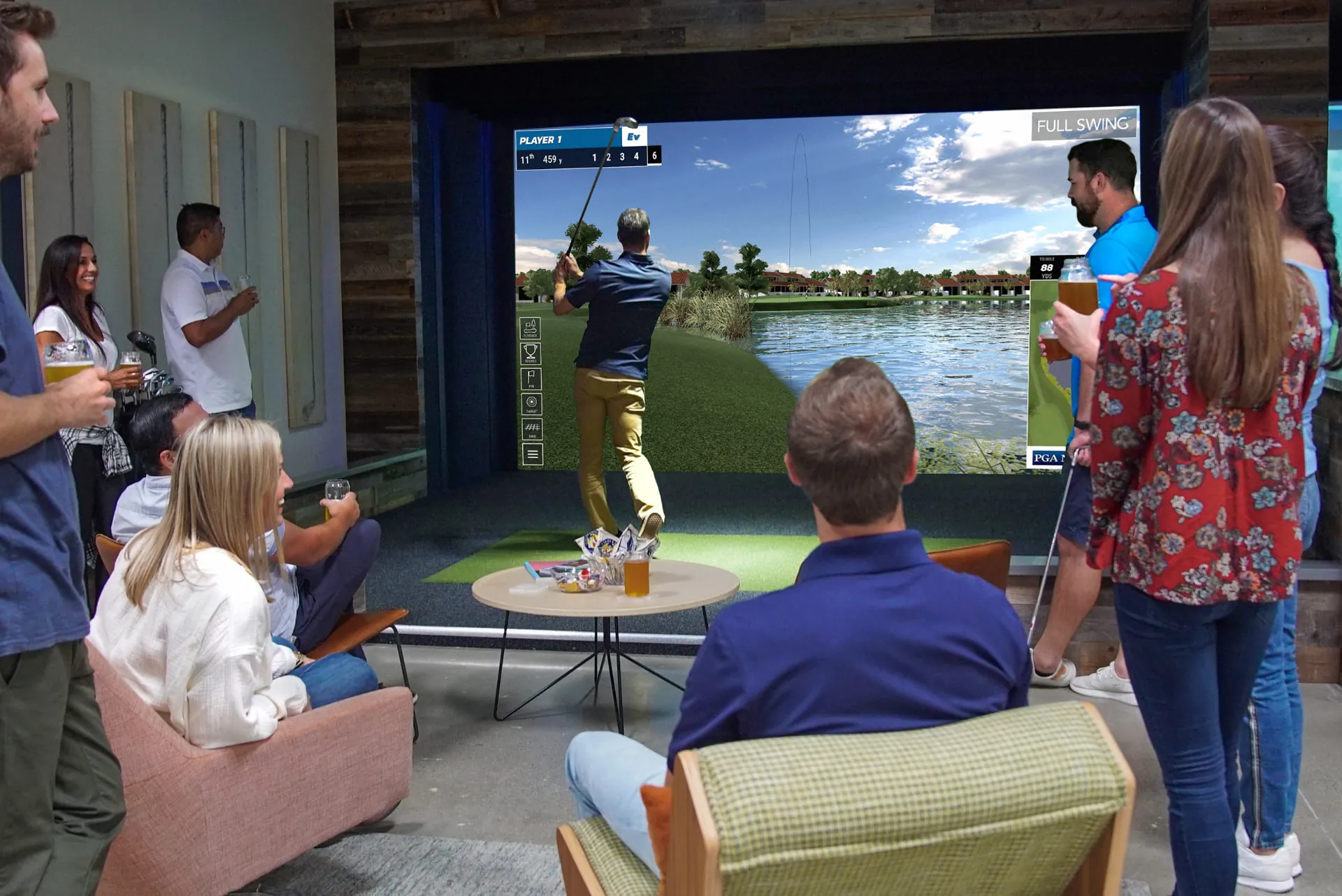 Group of coworkers gathered with drinks watching a teammate take a swing in an indoor golf simulator bay